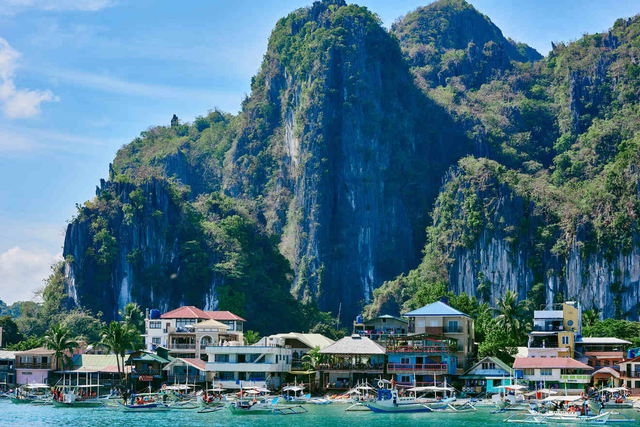 A bustling seaside village with colorful buildings along the shoreline, set against a backdrop of dramatic limestone cliffs and lush greenery.