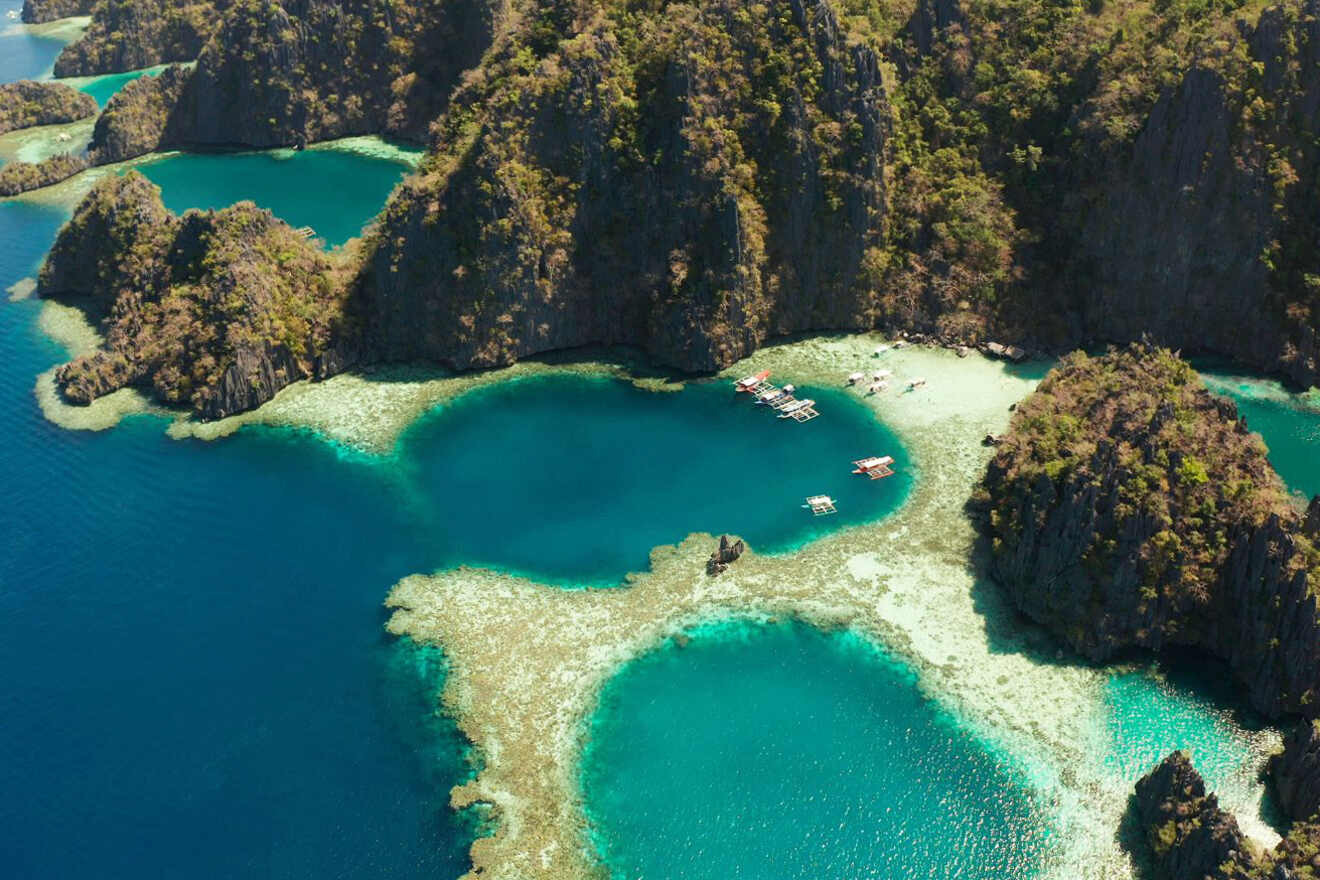 Aerial view of turquoise lagoons and limestone cliffs surrounded by dense vegetation, with several small boats anchored near the shore.