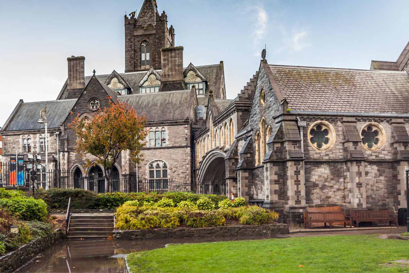 The intricate stonework and gothic architecture of Dublin's Christ Church Cathedral stand out on a cloudy day, with autumn-colored foliage in the foreground