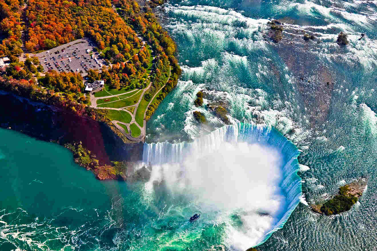 Aerial view of Niagara Falls with vibrant autumn foliage surrounding the cascading water and a tourist boat in the river.