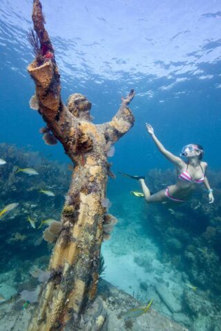 a girl in a swimming mask swims next to an underwater statue