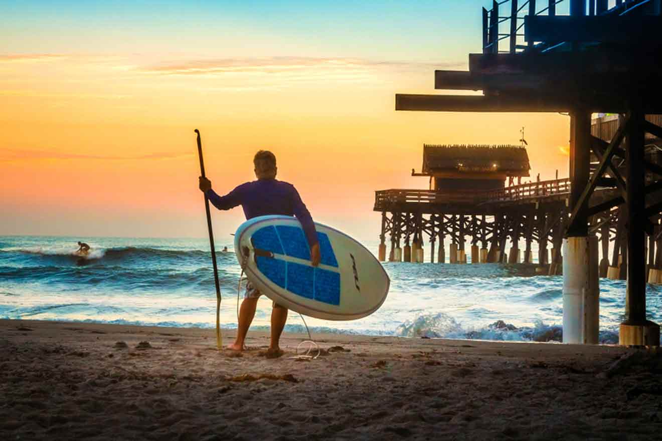 man sitting next to Cocoa beach pier with a surfing board in his hands
