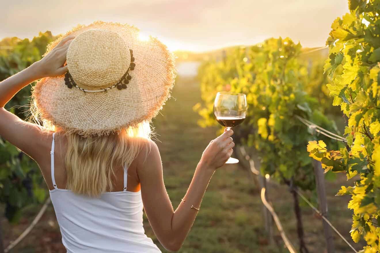 woman holding a glass of wine while watching over the sunset at a vineyard