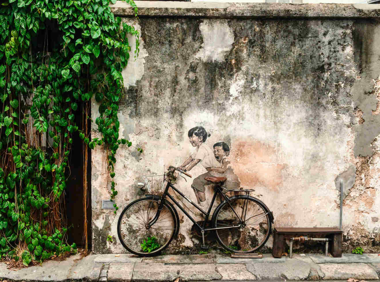 Street art in Penang: a mural of a boy and girl made to look like they are riding a real bicycle
