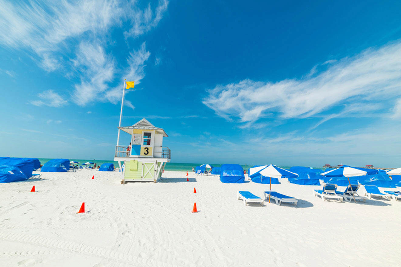 Vibrant beach scene with a lifeguard stand, blue umbrellas, white sand, and a clear sky