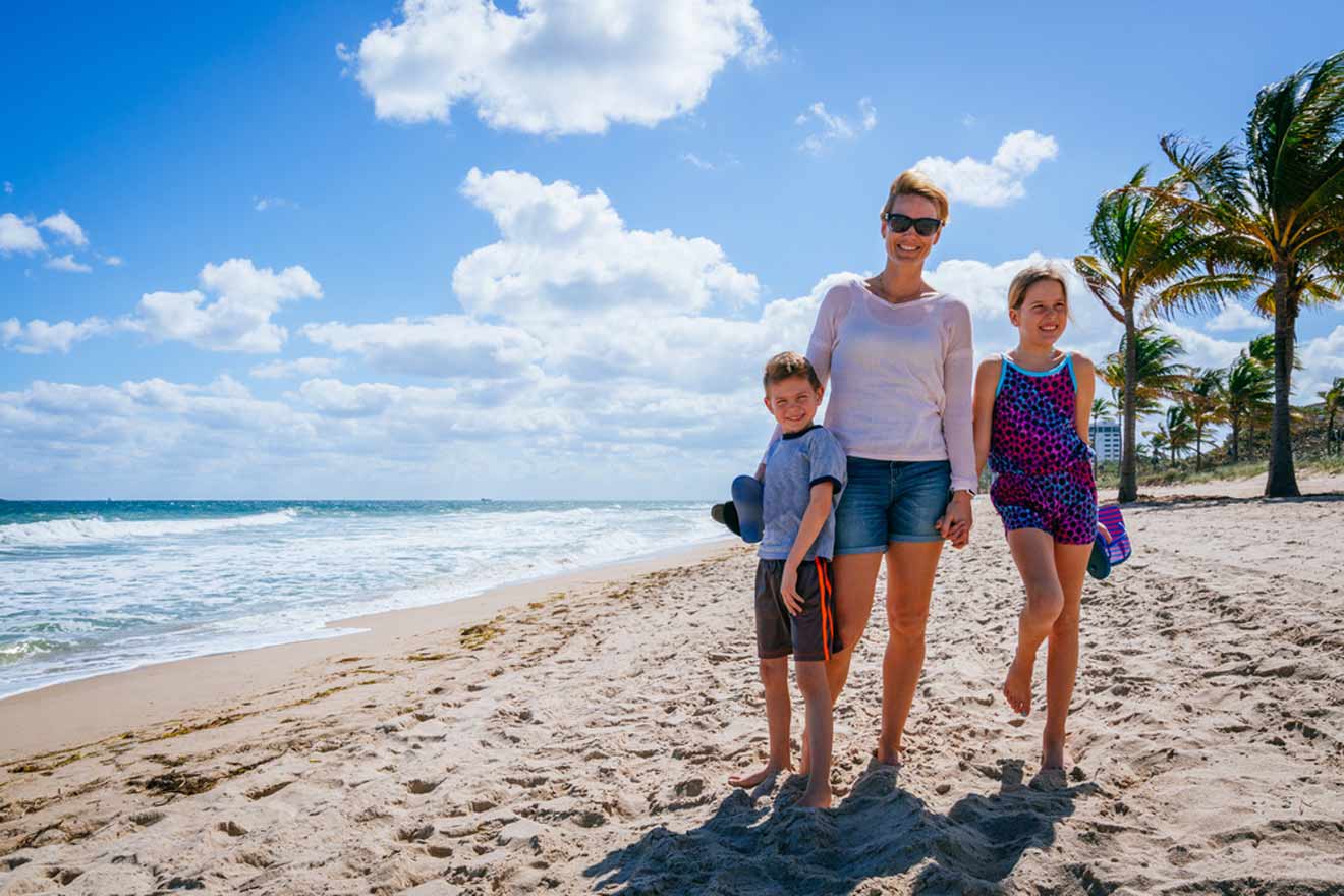 Family with two children walking on a sandy beach under a clear blue sky