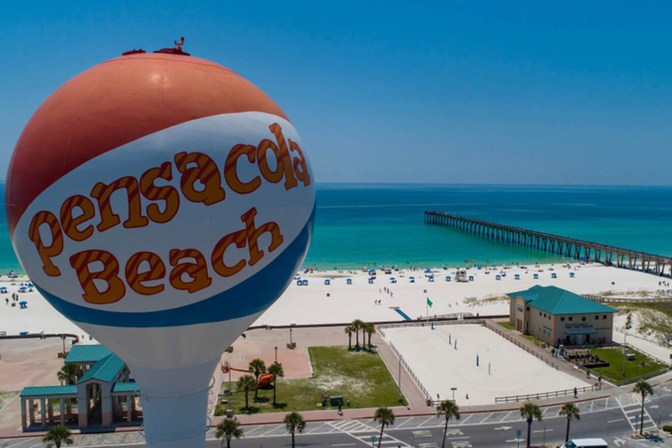 A big ball-shaped sign saying Pensacola Beach with the beach in the background