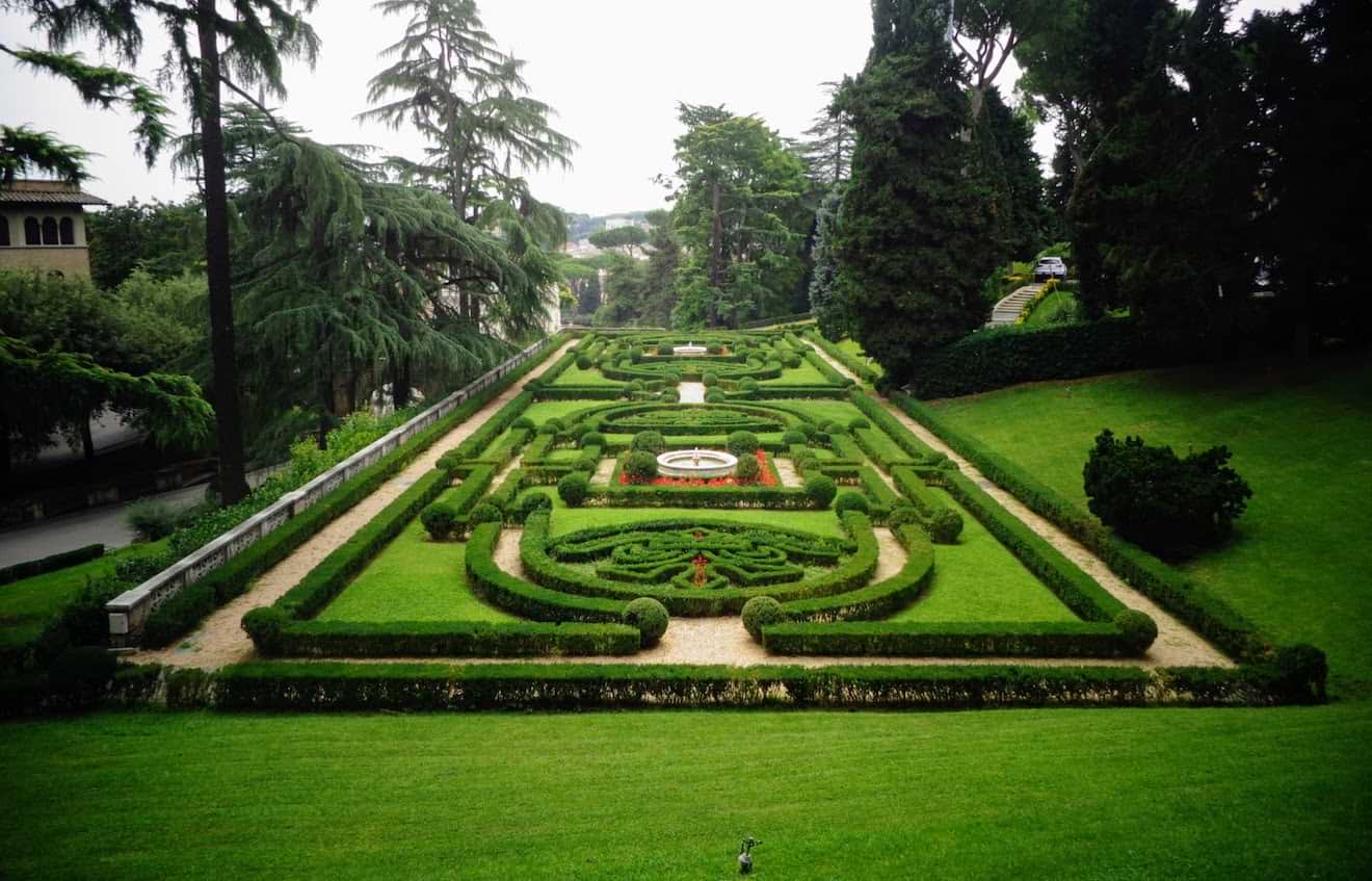 The meticulously manicured gardens of the Vatican with geometric hedges and green lawns.