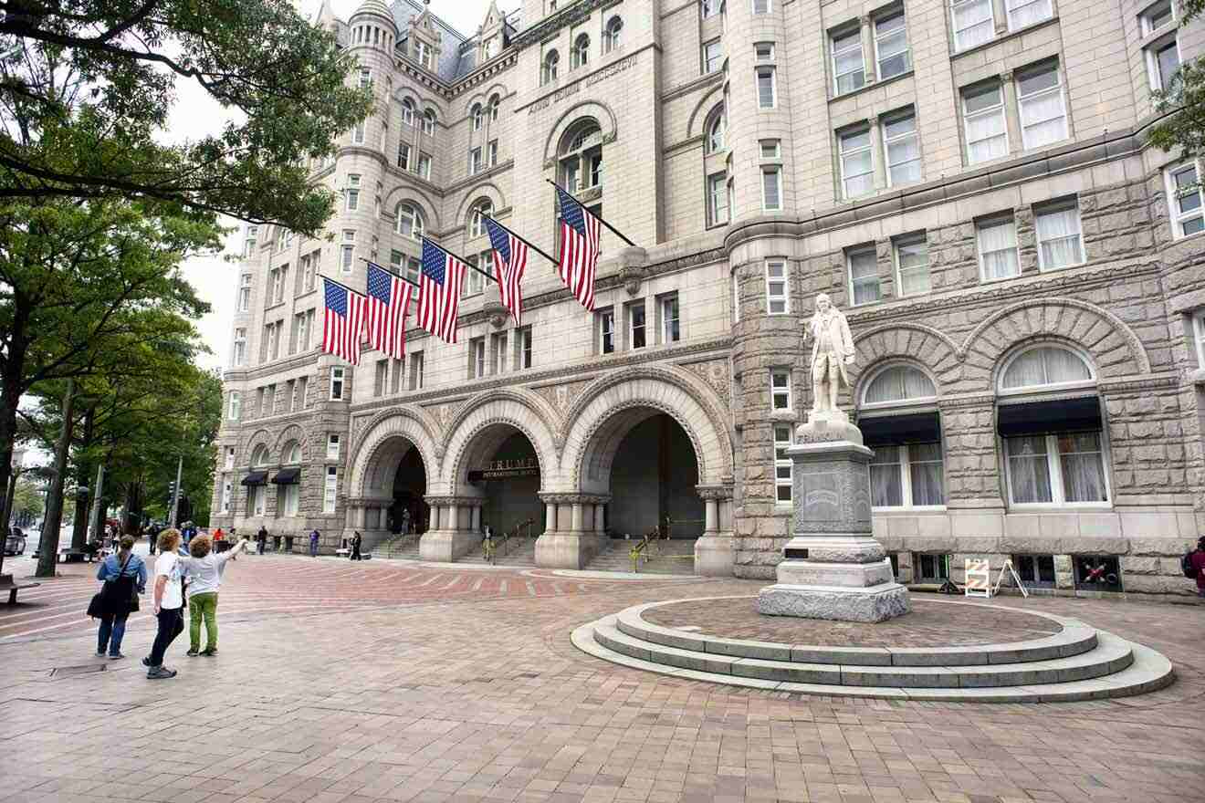 a group of people walking in front of a large building with USA flags