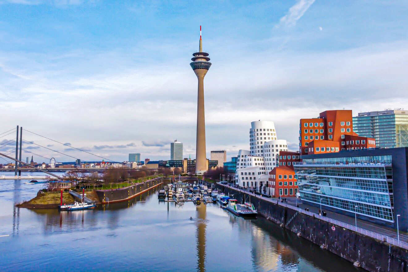 Cityscape of Düsseldorf with the Rhine River, featuring the Rheinturm tower and modern buildings along the waterfront.