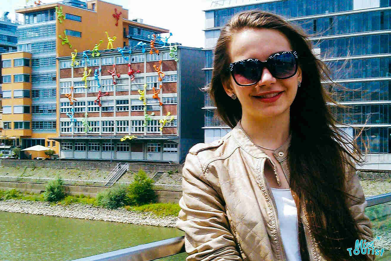 Beti wearing sunglasses poses in front of a colorful building with large, climbing sculptures.