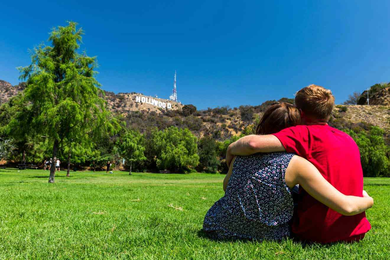 couple sitting on the grass looking over the Hollywood Sign