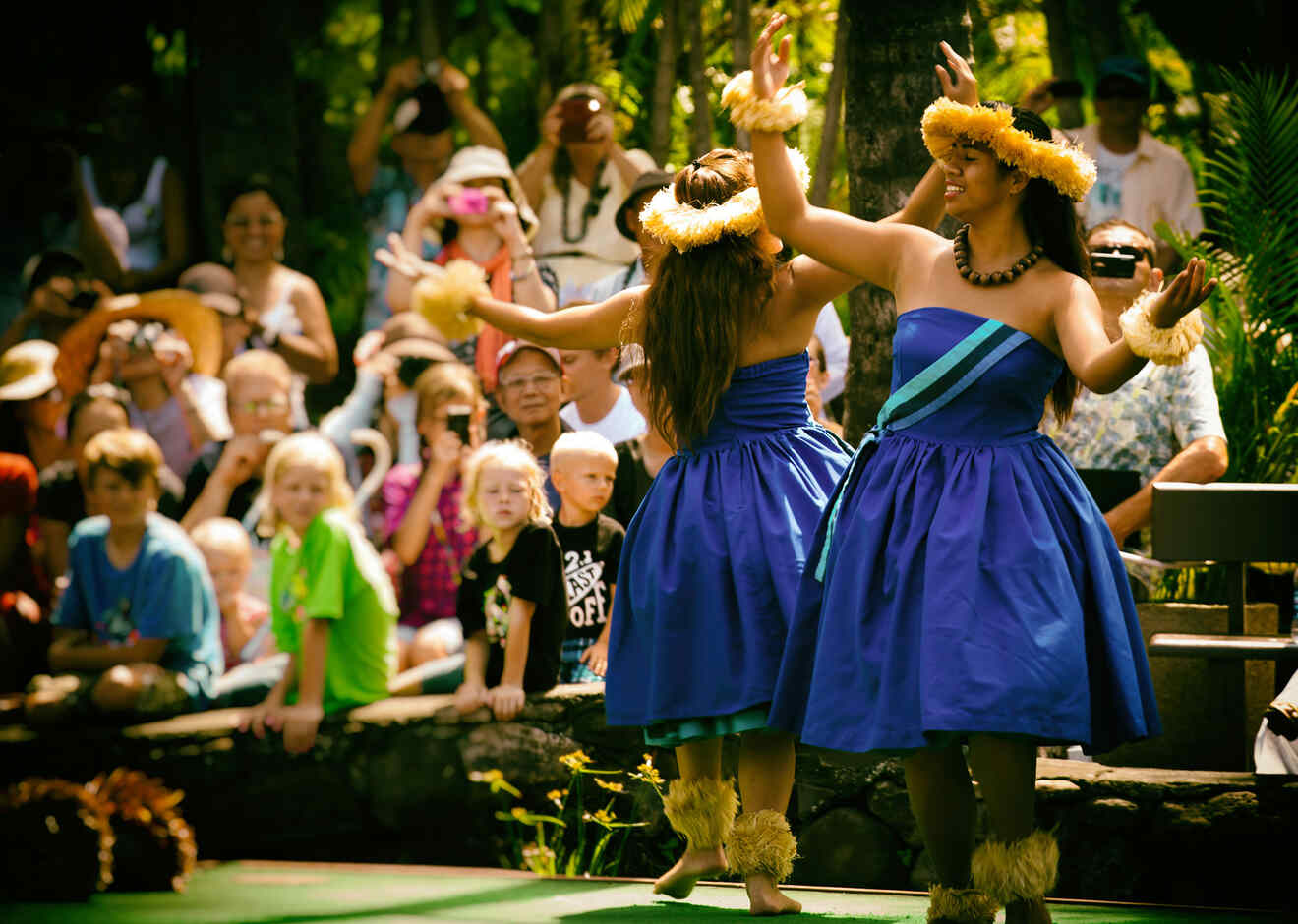 People watching women in traditional wear dancing at luau