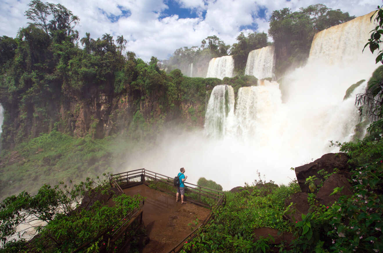 A man standing on a bridge in front of a waterfall