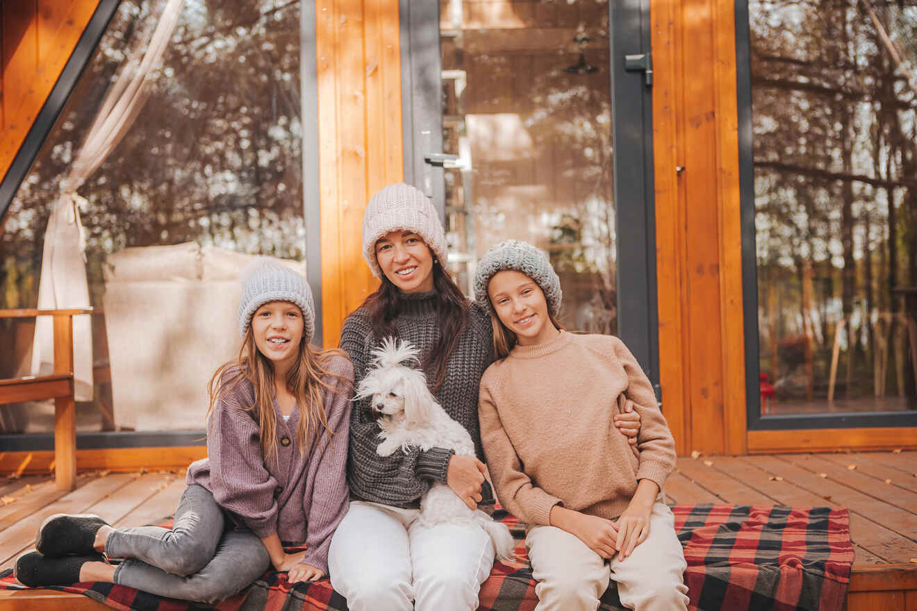 Two girls and a woman holding a dog sitting on cabin's deck