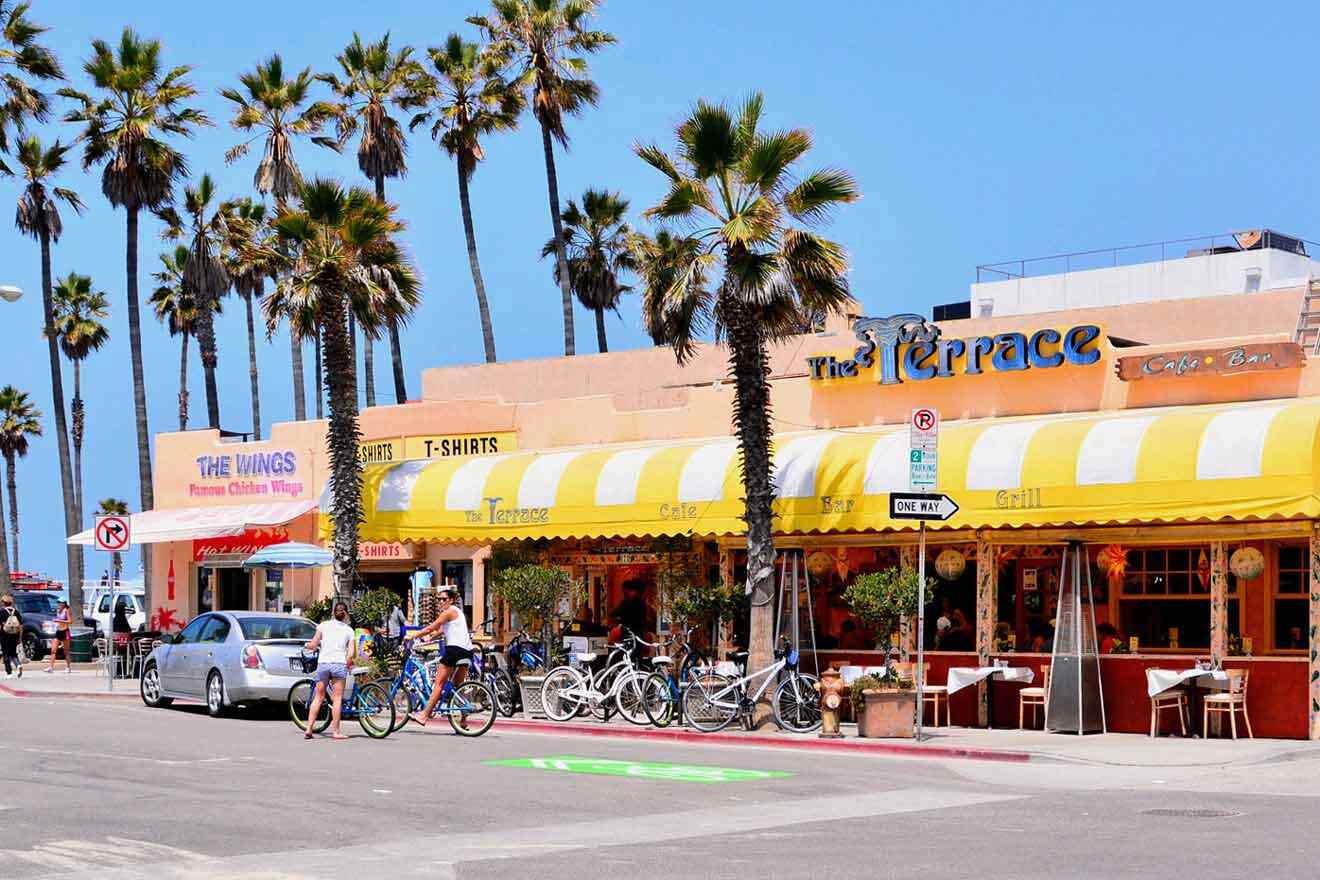 a couple of people riding bikes down a street in front of a cafe