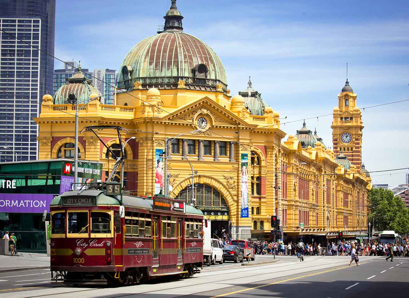 a tram passing in front of a yellow building with a dome on a crowded street