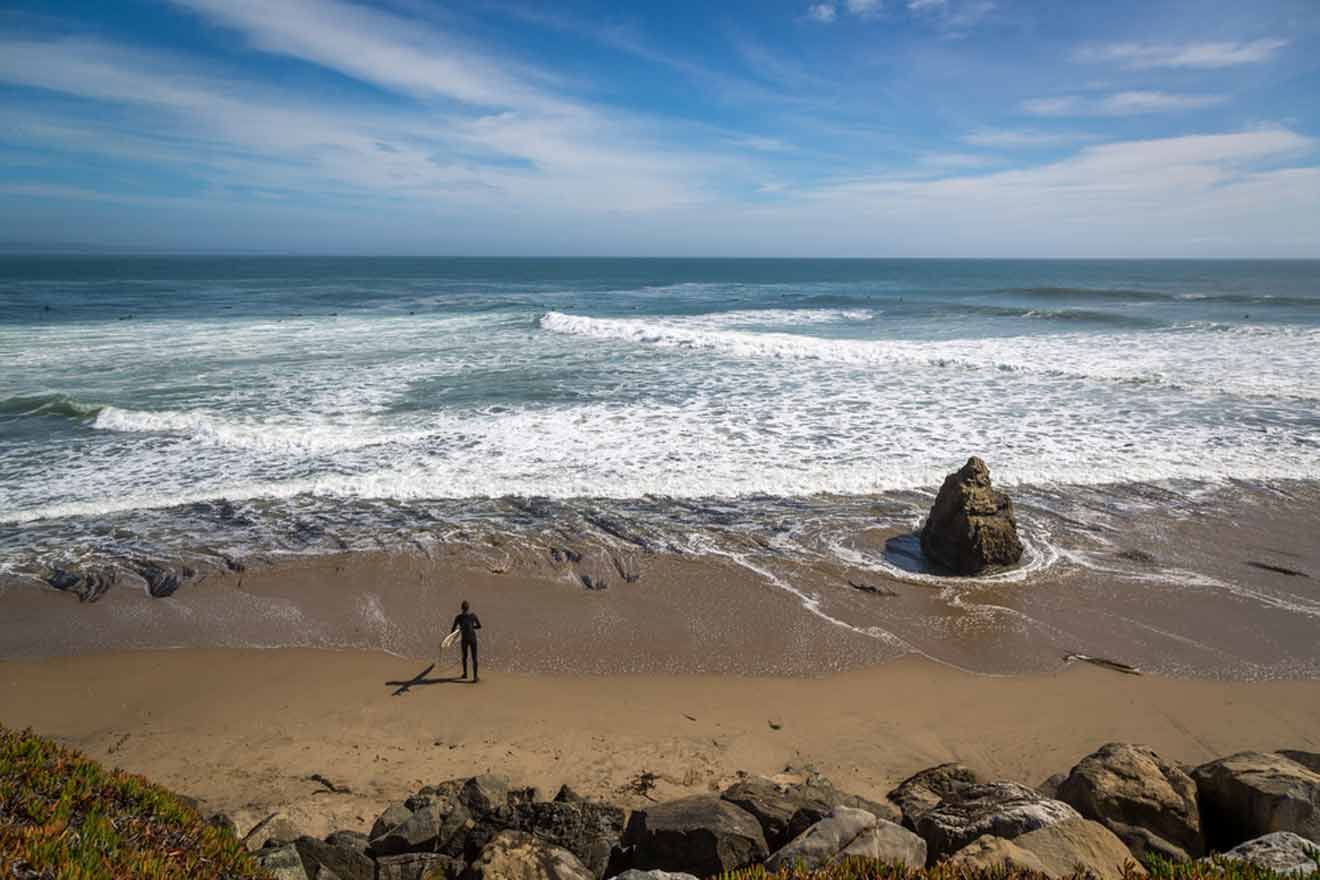 a person standing with a surf on a beach next to the ocean