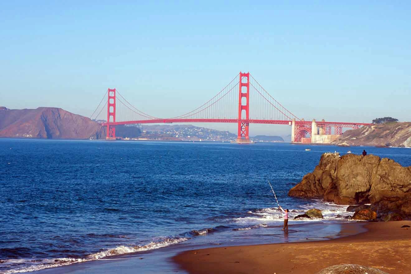 a person standing on a beach next to a body of water with a view of the golden gate bridge
