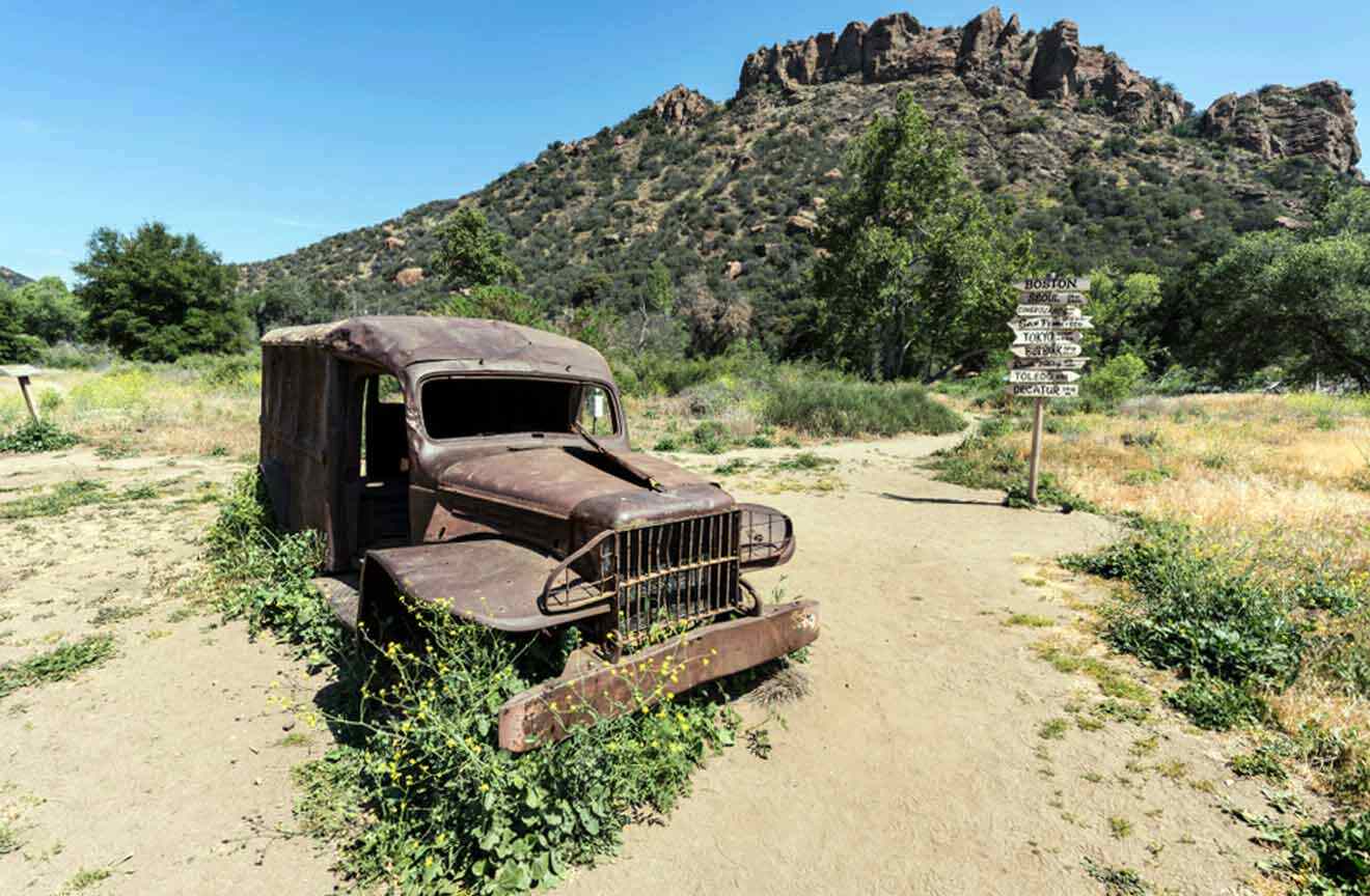 an old truck sitting in the middle of a dirt road