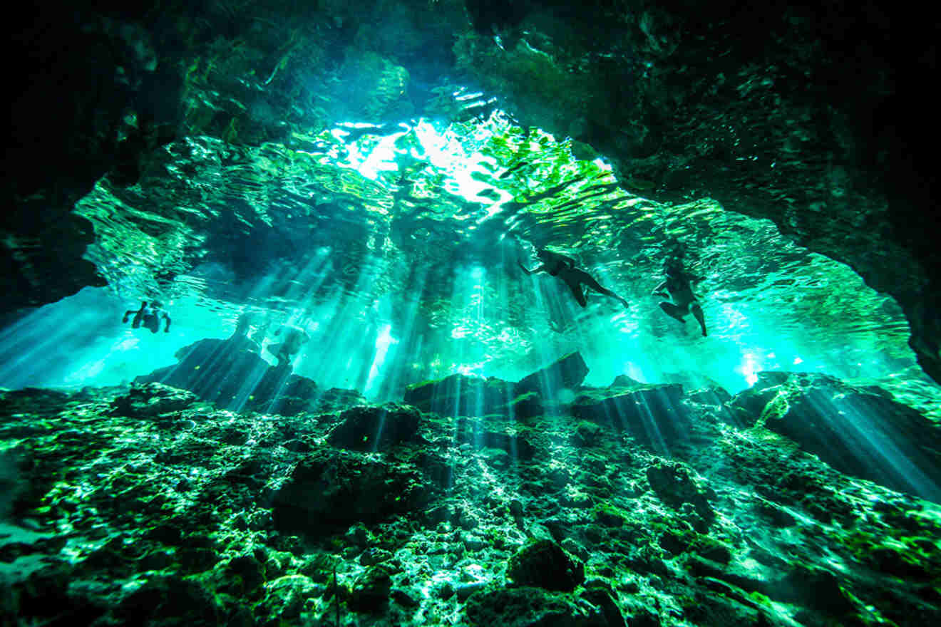 a cave with sunlight streaming through the ceiling and people swimming and snorkeling