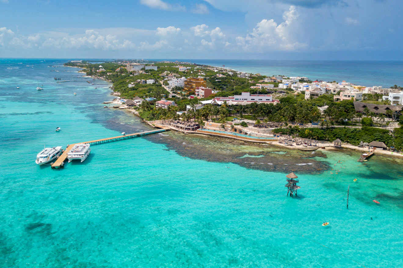 Aerial shot of a bustling pier in Isla Mujeres, Cancun, with boats docked along the clear turquoise waters of the Caribbean Sea, overlooking a vibrant coastal community.