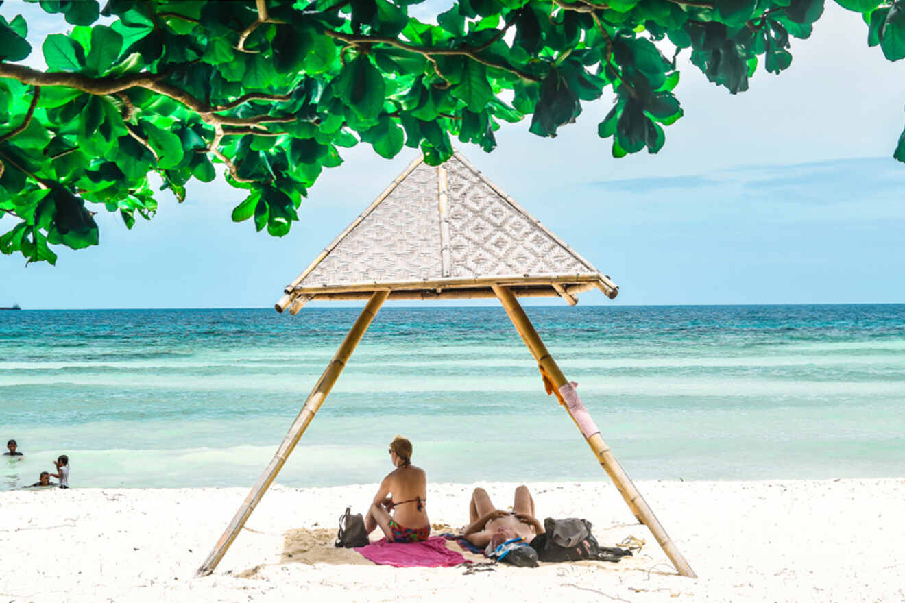 couple sitting on a beach under a wooden umbrella