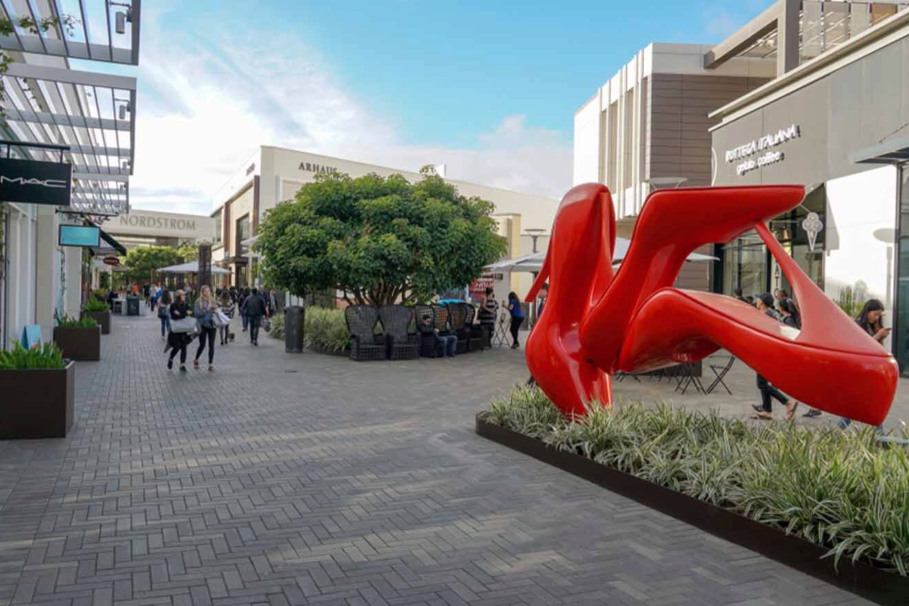 view of a street with lots of shops and greenery with a shoes statue