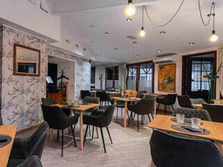 Modern cafe interior with wooden tables, black chairs, hanging light bulbs, and artwork on the walls.