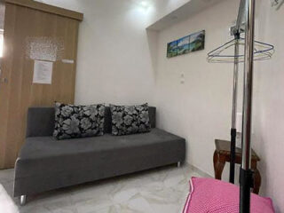 A small room with a gray sofa, floral cushions, a sliding door, a landscape picture on the wall, and a clothes rack with a pink cover.