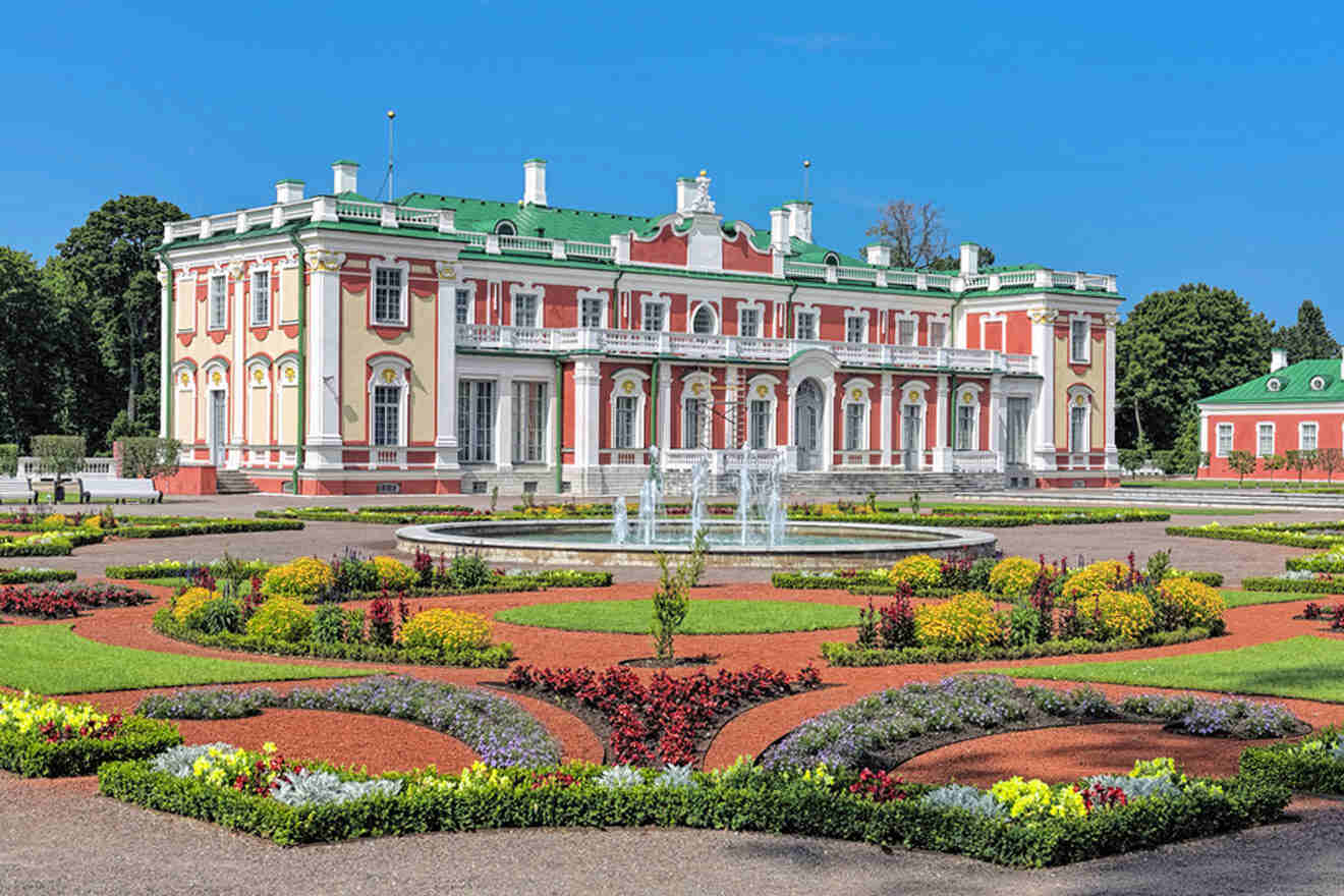 a palace with a fountain and lots of flowers and plants in front of it