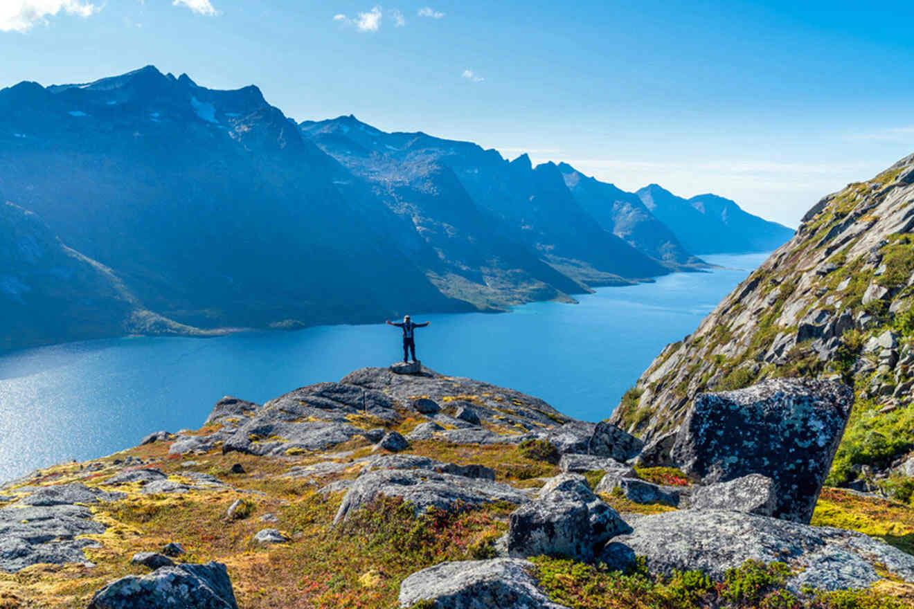 a man standing on top of a mountain next to a lake