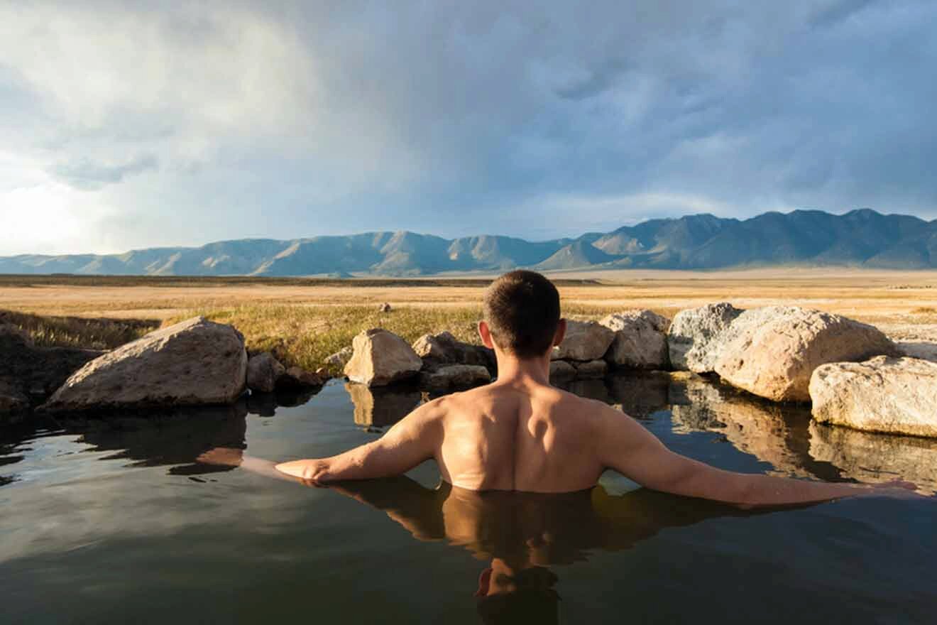 a man sitting in a hot spring with mountains in the background