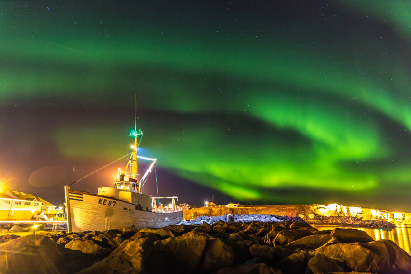 boats in the harbour with rocks and aurora borealis on the sky