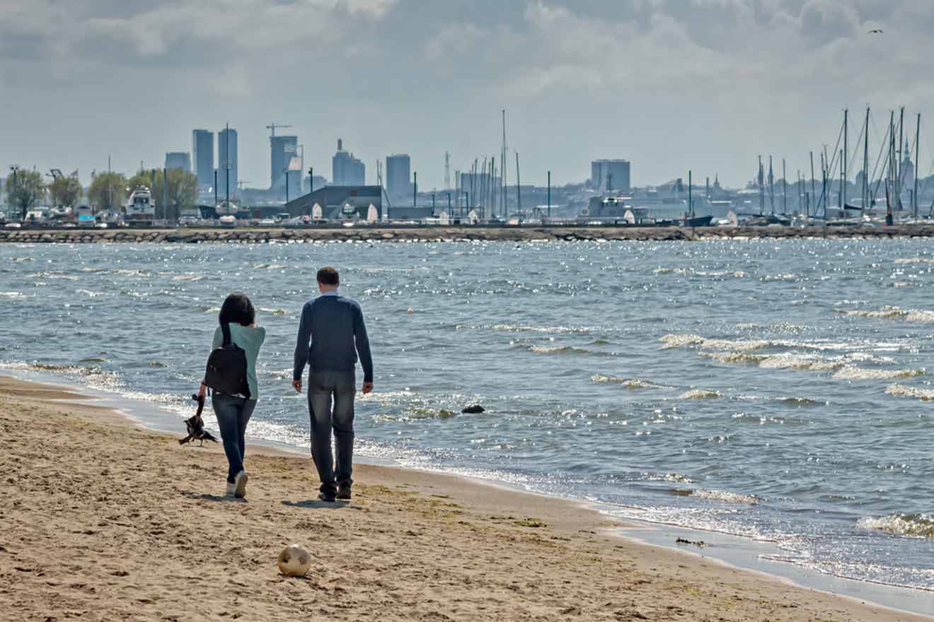 a man and woman walking on a beach with a city in the background