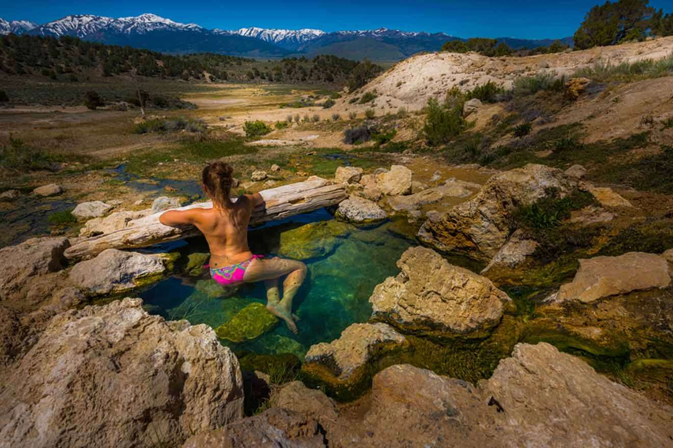 a woman sitting on top of a rock next to a body in a hot spring