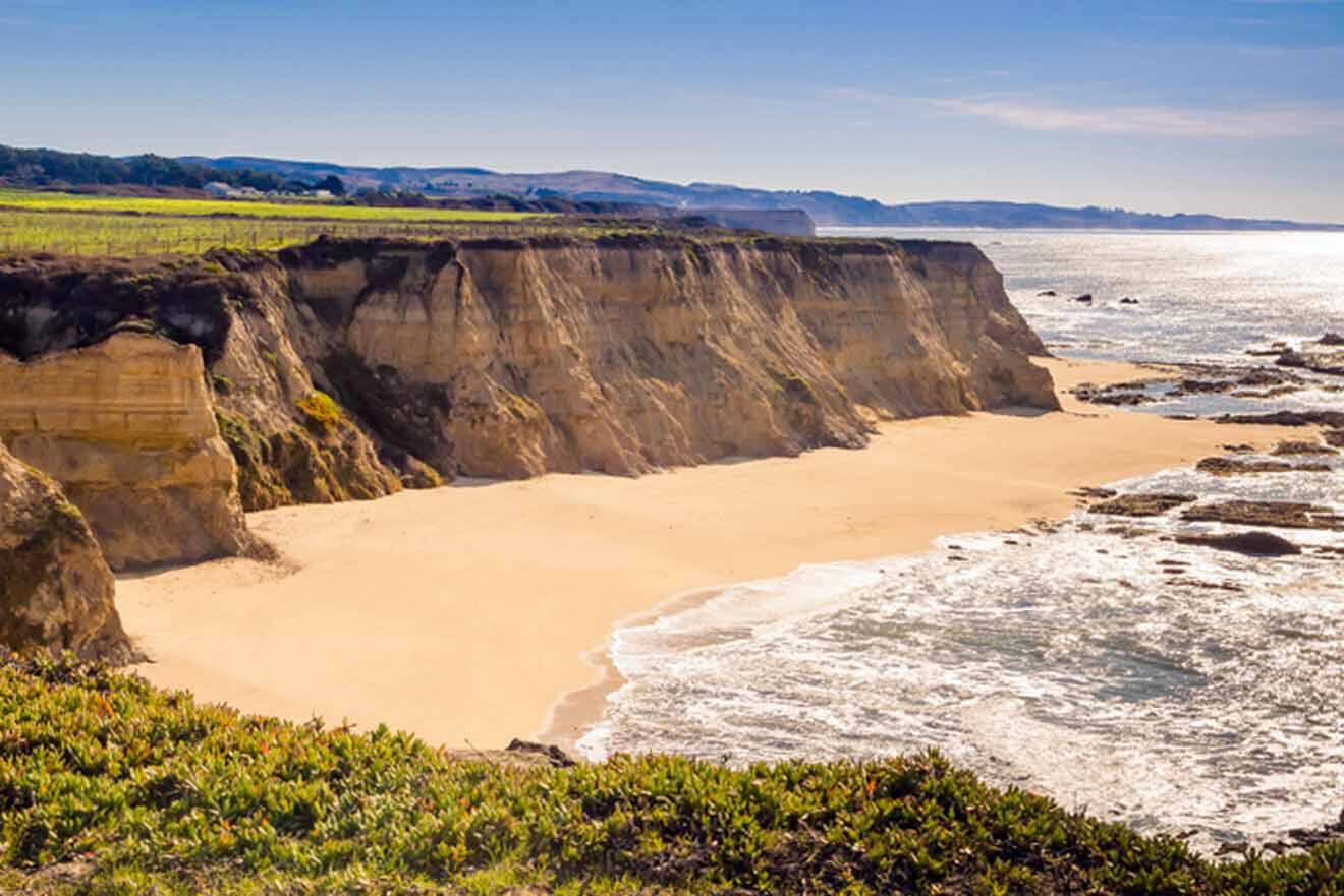 a sandy beach next to a cliff on a sunny day