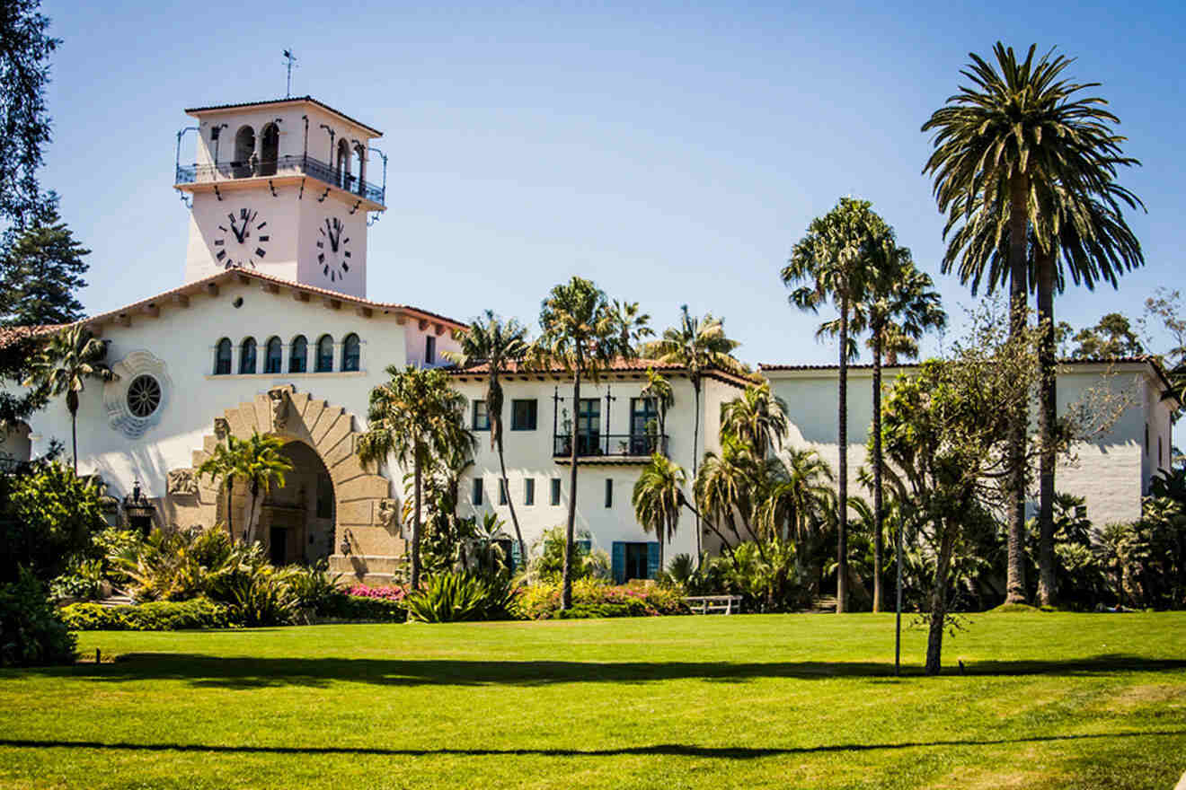 a large white building with a clock tower surrounded by grass and palm trees