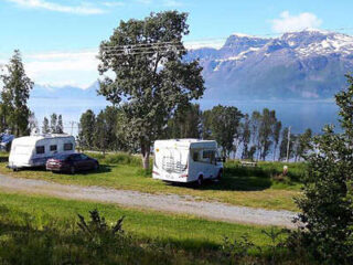 a couple of parked campervans on a field in front of a lake and snowy mountains
