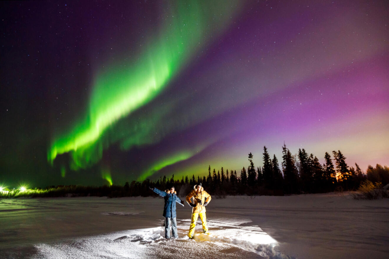 tourists on a snowy field watching the aurora borealis
