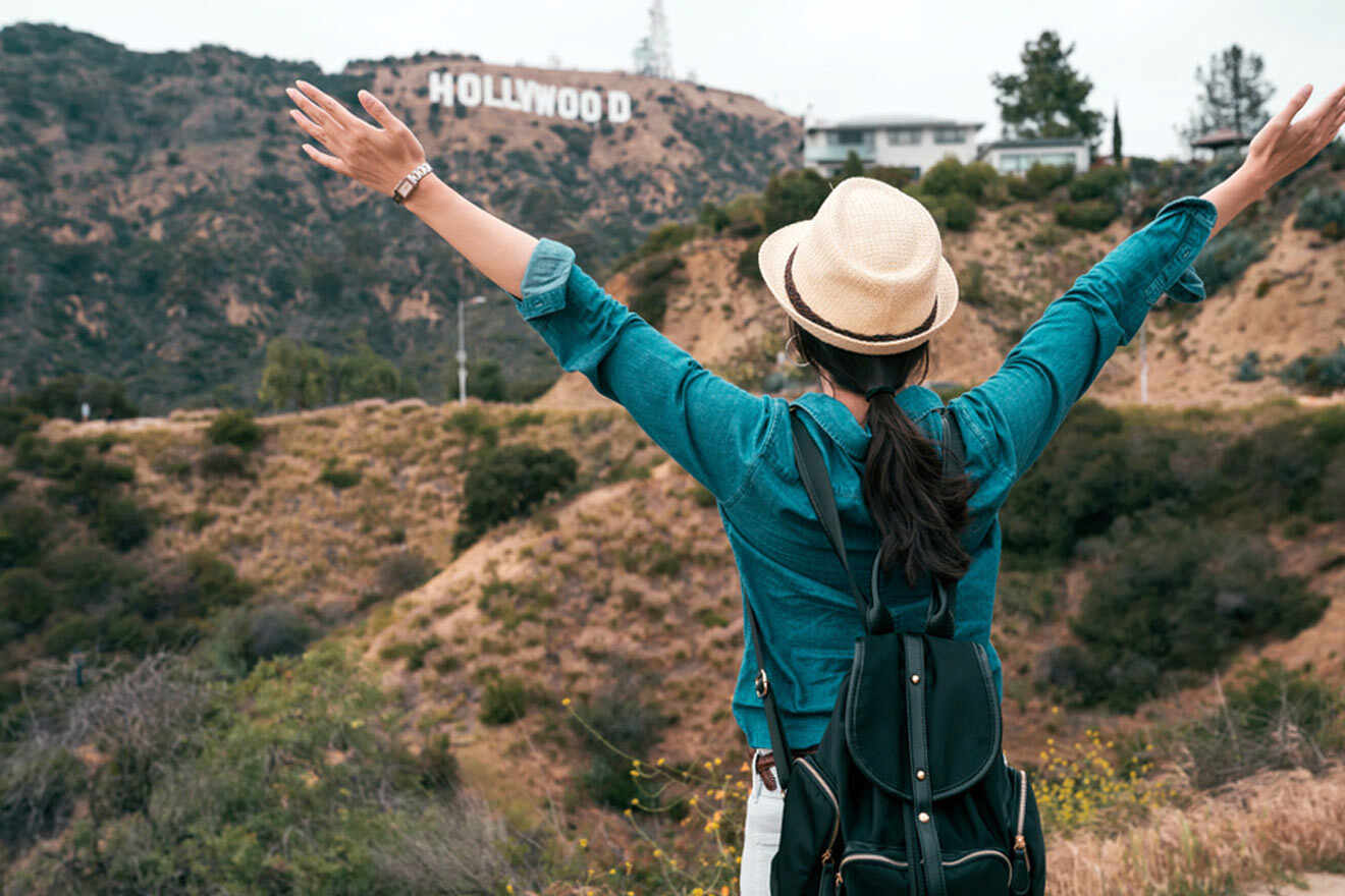 a woman with her arms outstretched in front of the hollywood sign