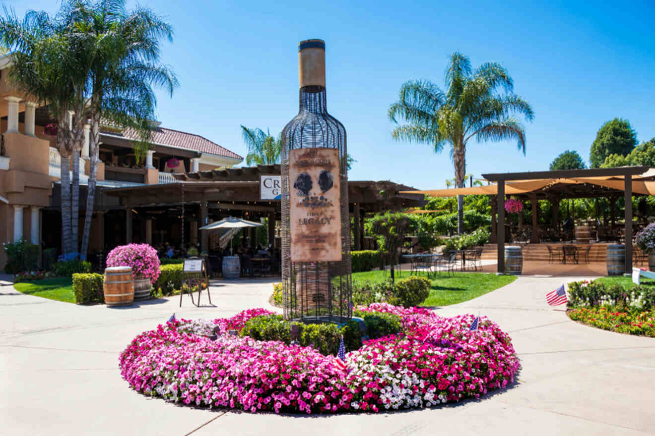 wine bottle statue surrounded by flowers and restaurant in the background