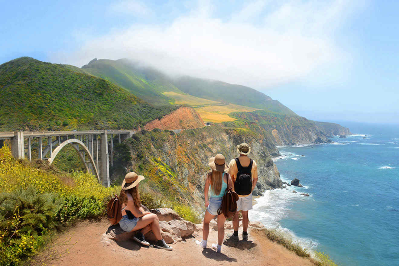 three people standing on a cliff overlooking the ocean