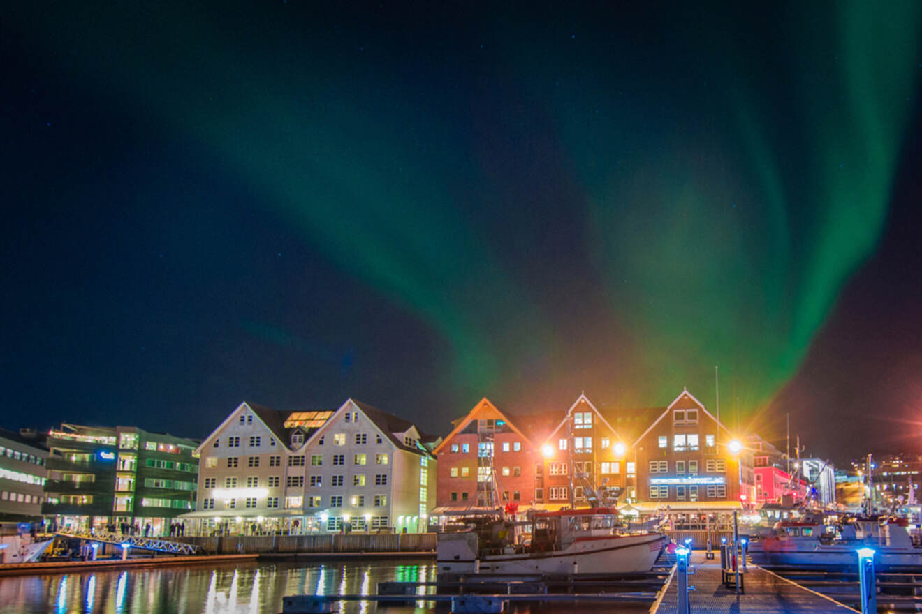boats in the harbour at night with the northern lights on the sky