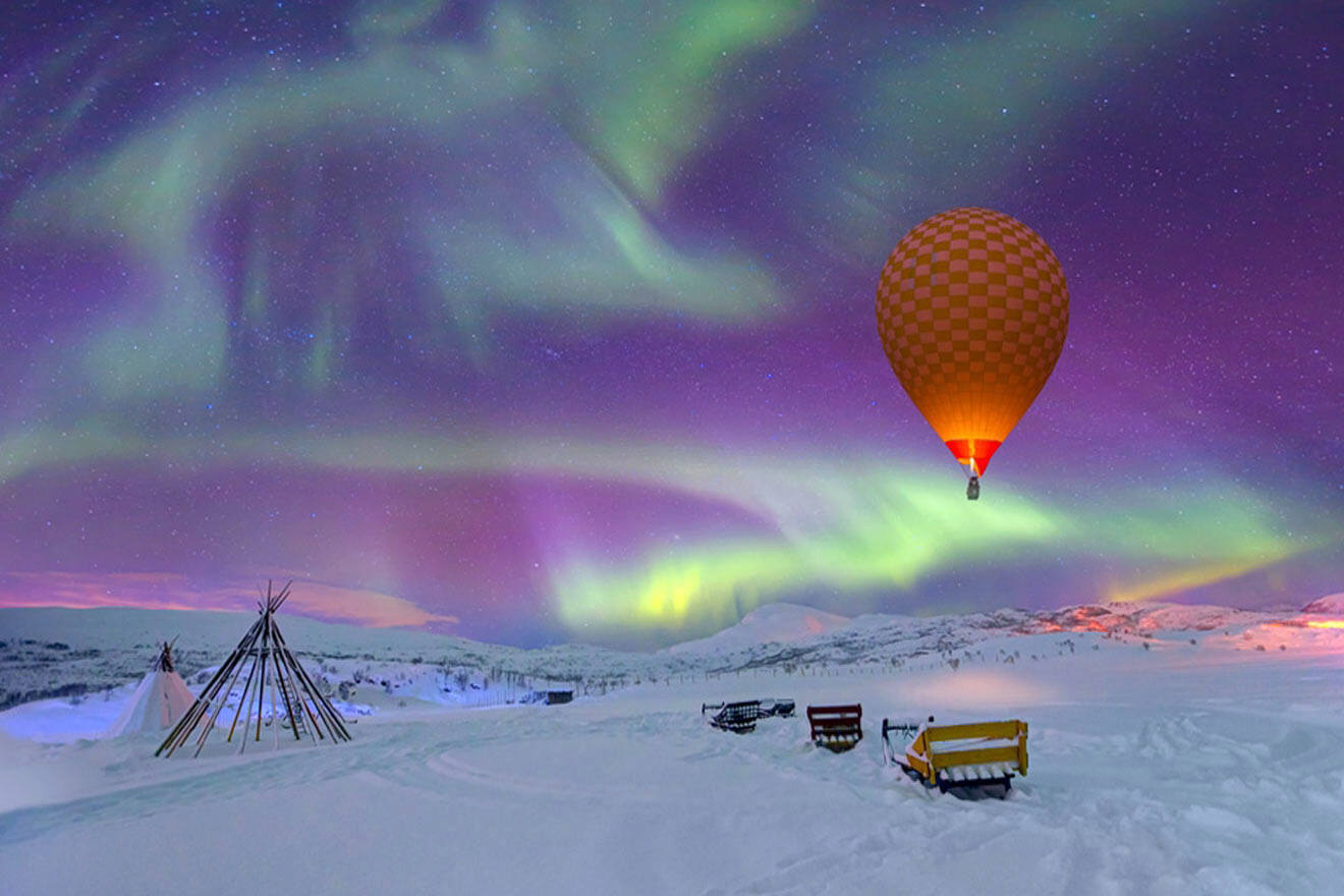 a hot air balloon flying over a snow covered field and aurora borealis in the sky