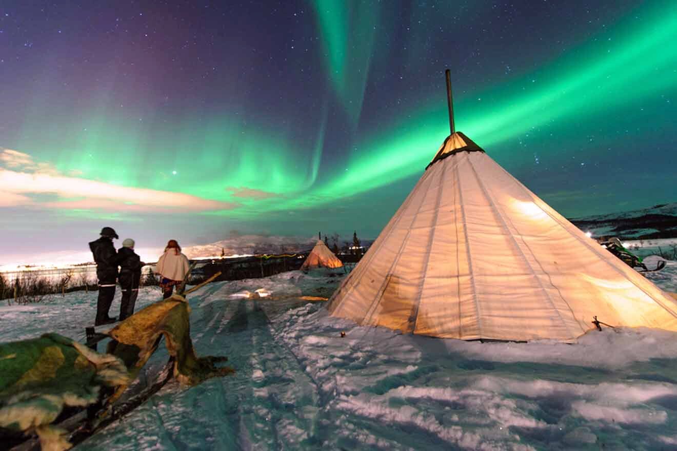 three people standing in front of a teepee with the aurora lights in the background