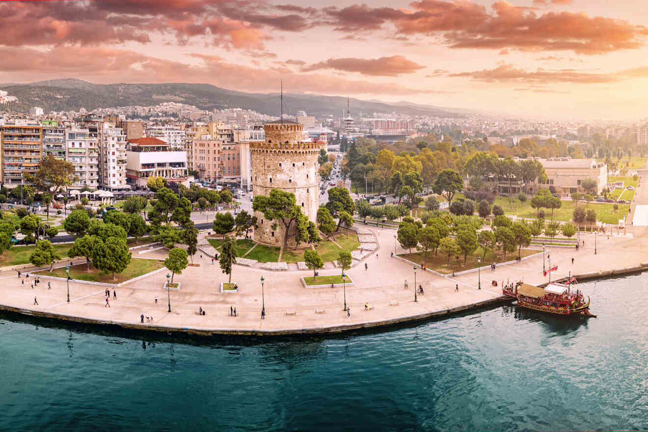 Sunset view of the White Tower of Thessaloniki, a historic fortress and museum, with the cityscape and waterfront promenade.
