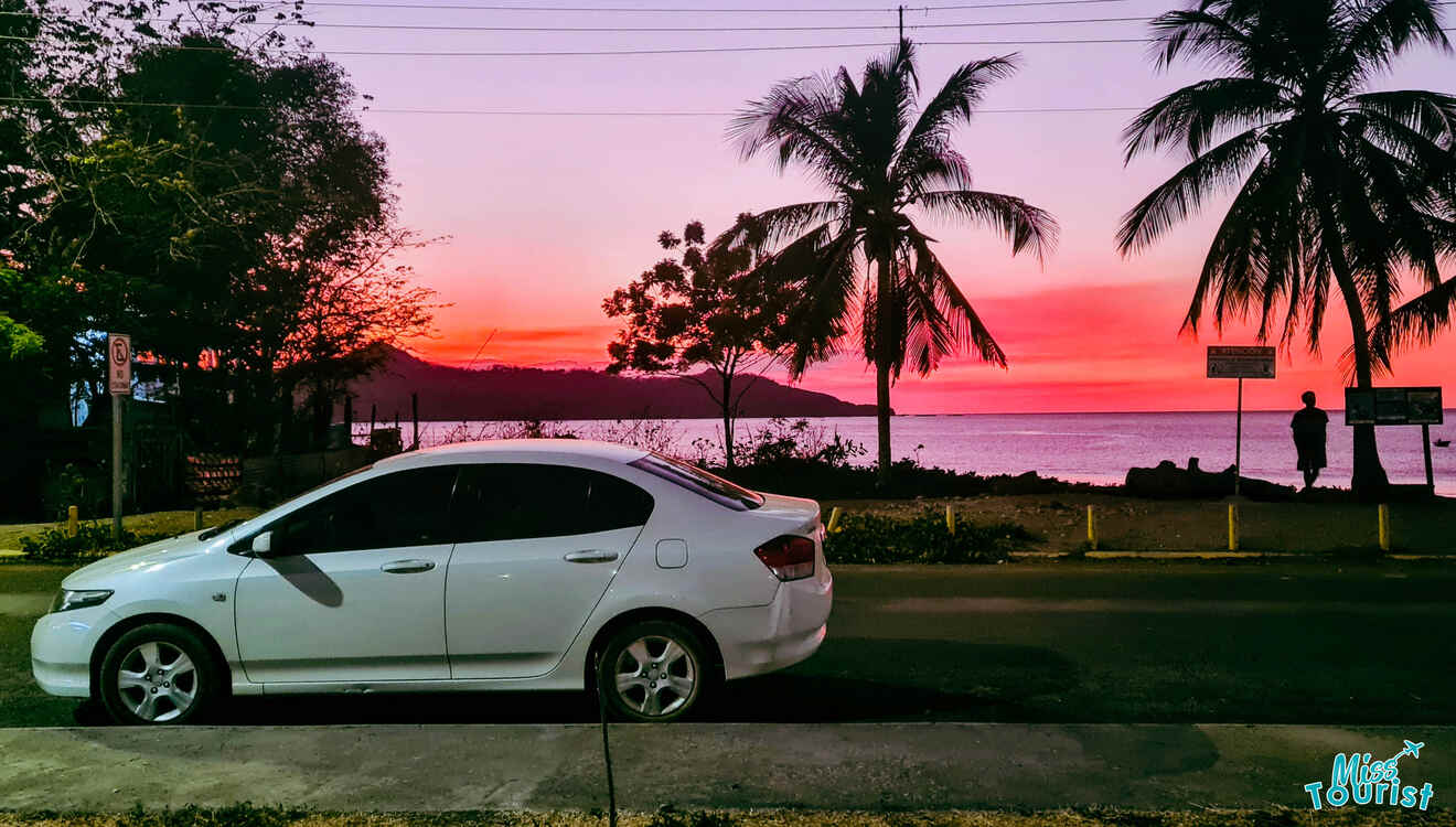 A white car parked on the side of the road at sunset.