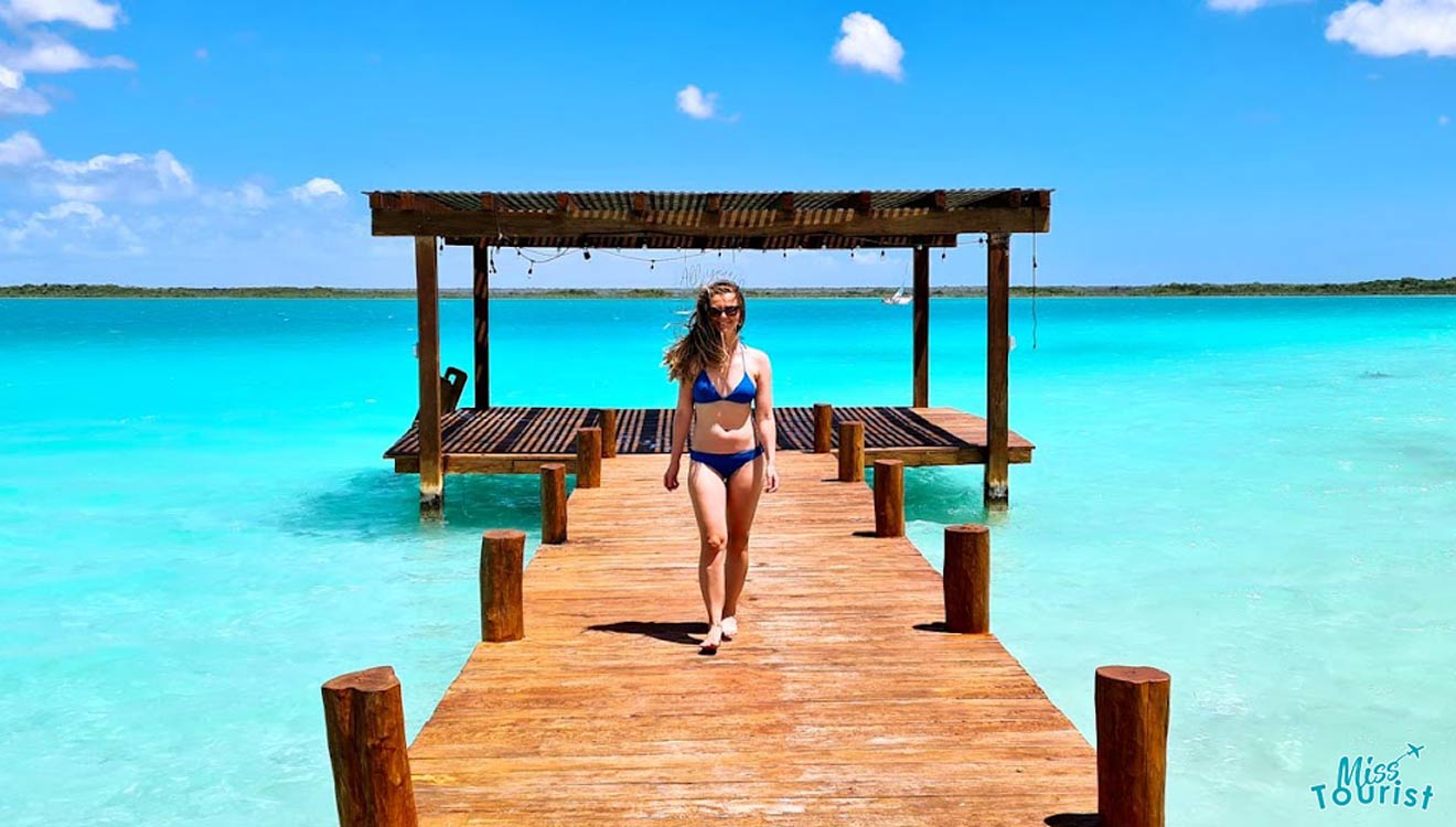 a woman in bikini walking on a wooden pierce over the water