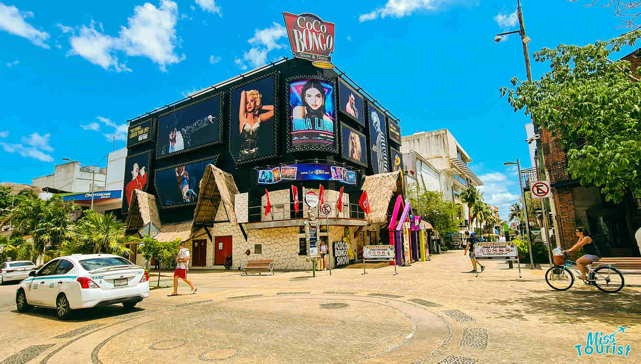 The lively entrance of Coco Bongo nightclub in Cancun, with large billboards featuring performers, under a bright blue sky, capturing the dynamic street life and local attractions